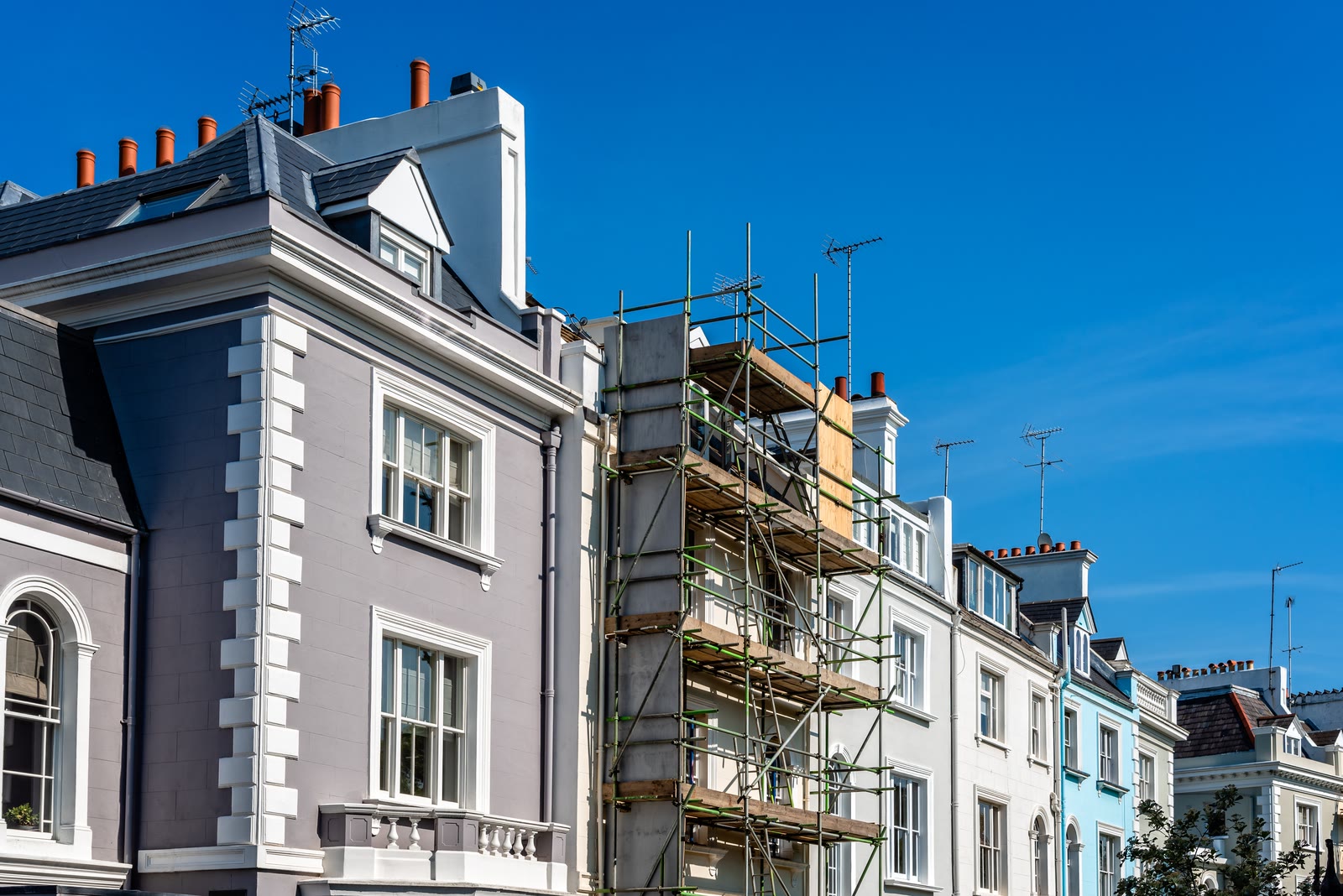 Townhouses under renovation with scaffolding against a blue sky